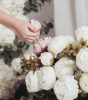 Hands arranging white peonies in a bouquet